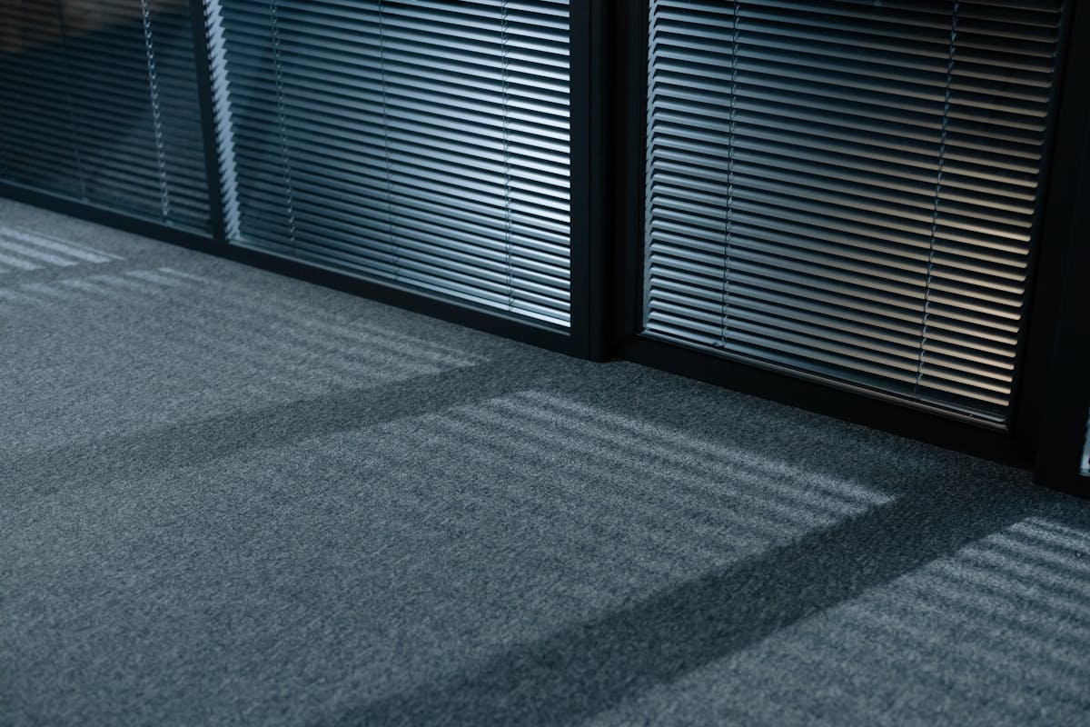 A serene indoor space with shadows and venetian blinds casting lines on a carpeted floor.