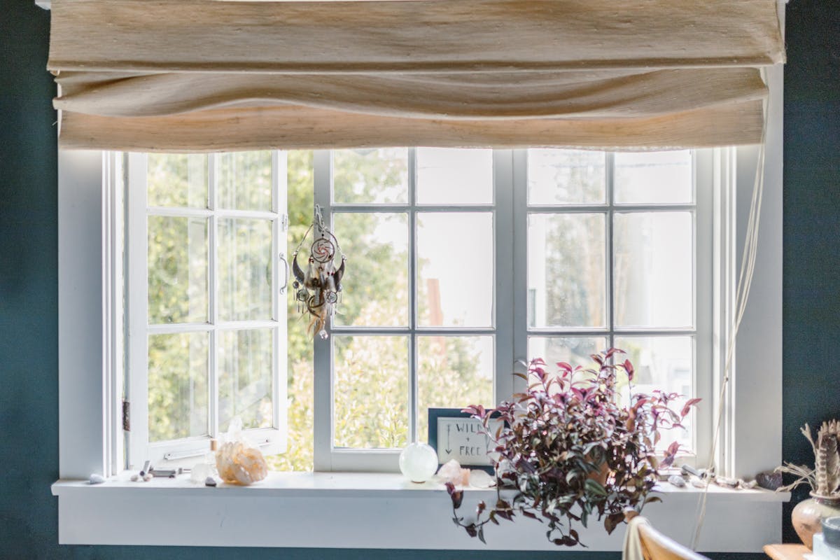 A serene indoor window scene with a dreamcatcher, crystals, and potted plant.