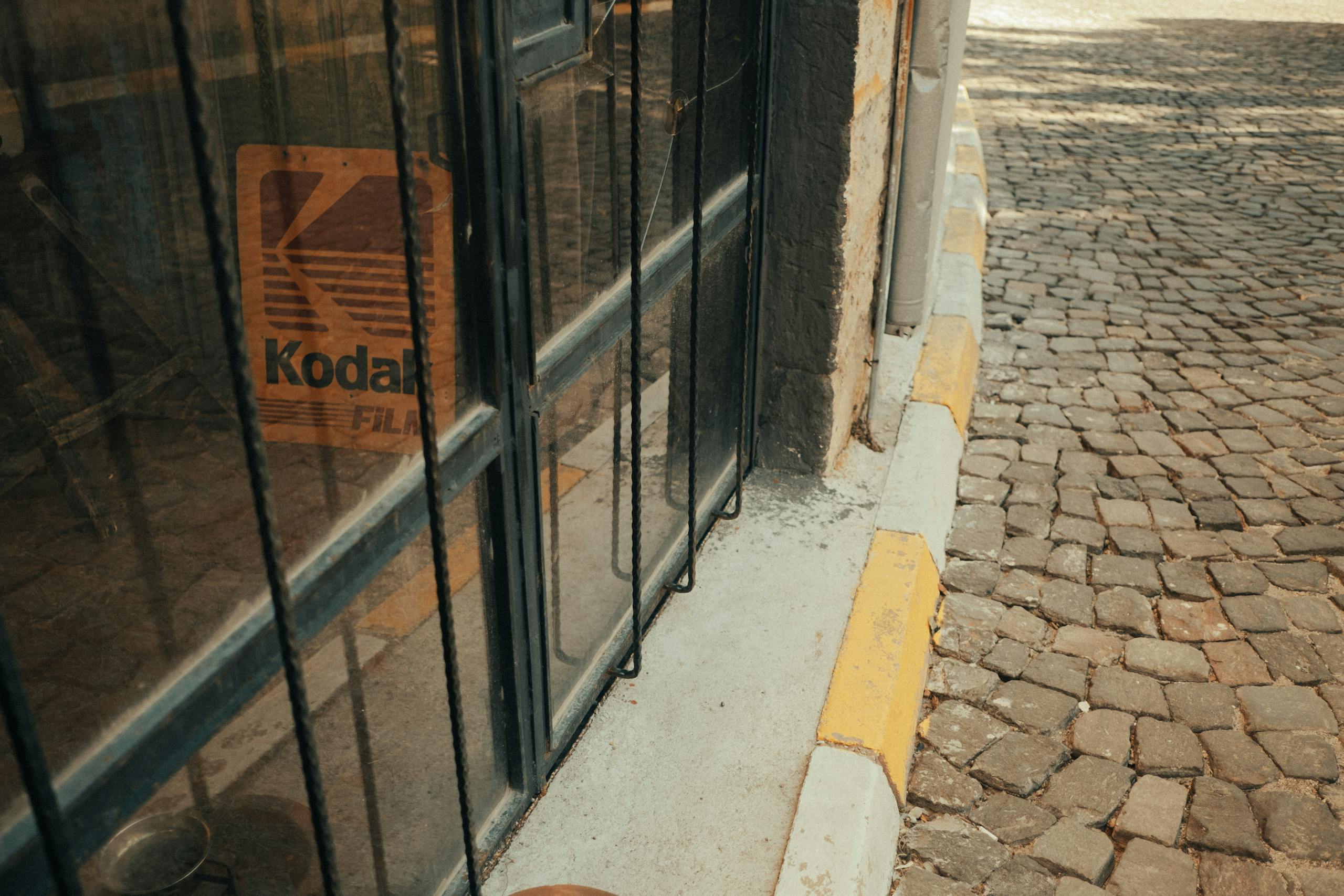 A vintage storefront with a Kodak sign, set against a cobblestone street with warm tones.