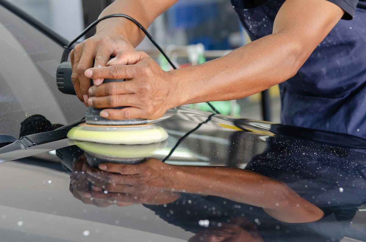 Detailed view of a worker's hands polishing a car's hood using a buffer in an auto workshop. ppf lifespan arizona