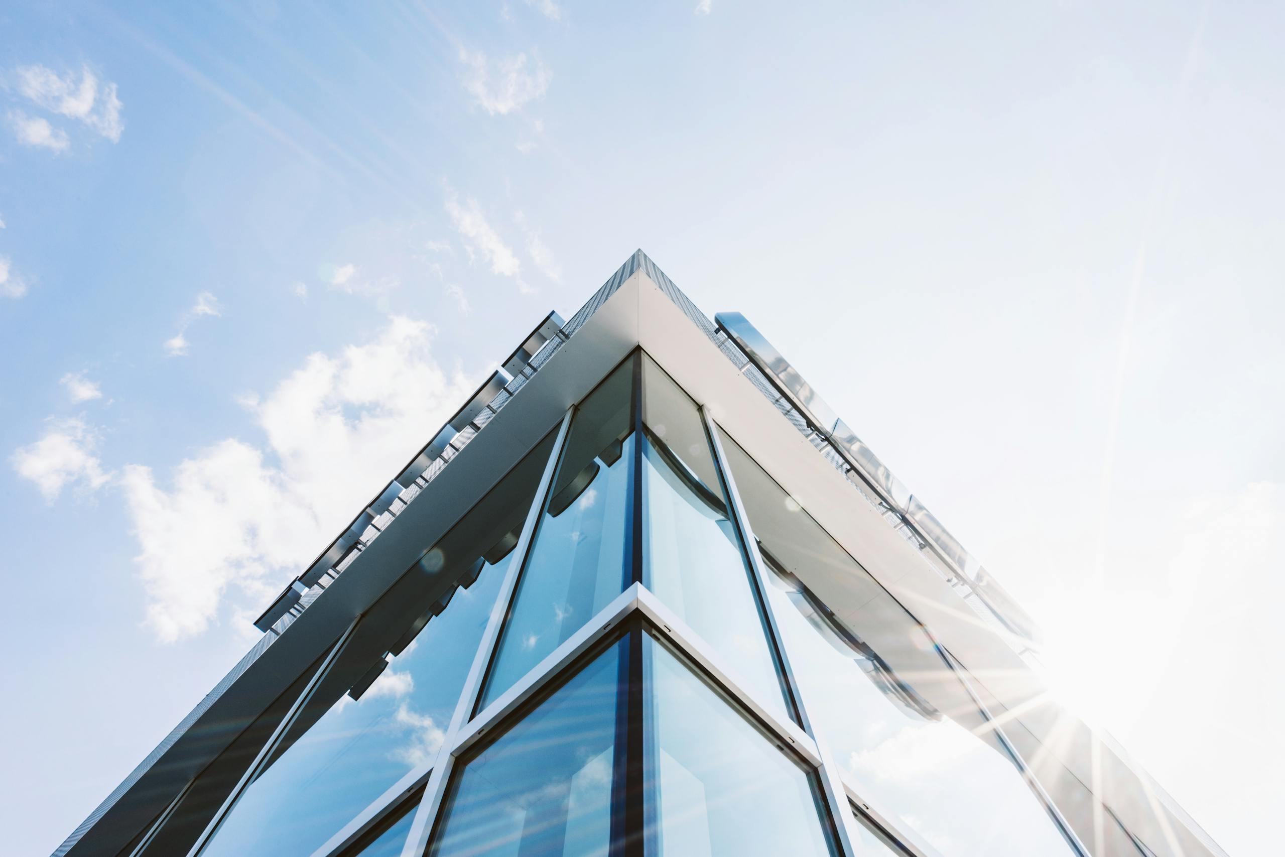 Low angle shot of a modern glass building with sun glare reflecting on its surface.
